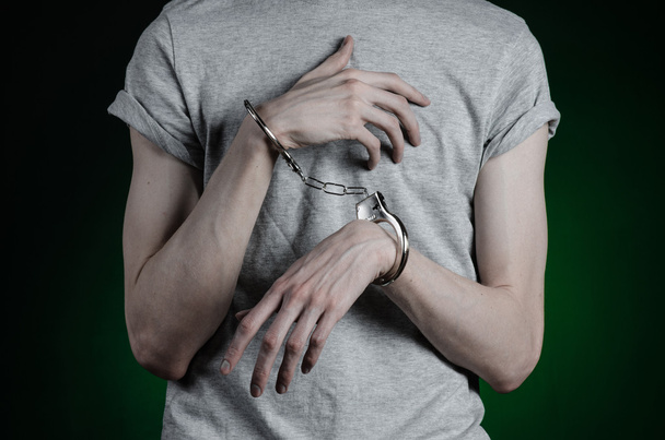 Gefängnis und verurteiltes Thema: Mann mit Handschellen an den Händen in grauem T-Shirt und blauer Jeans auf dunkelgrünem Hintergrund im Studio, legt Drogendealer Handschellen an - Foto, Bild