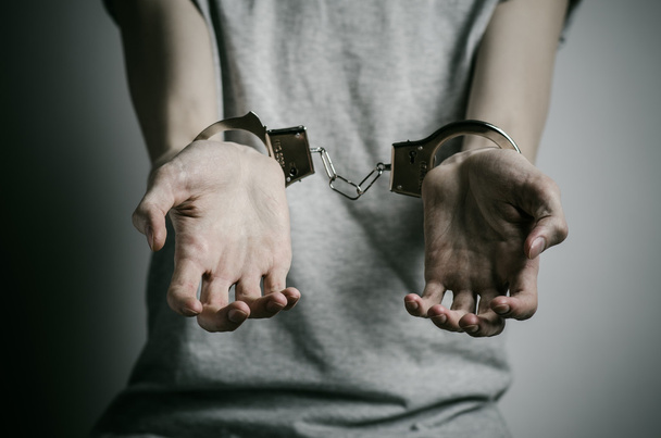 Prison and convicted topic: man with handcuffs on his hands in a gray T-shirt on a gray background in the studio, put handcuffs on rapist - Фото, зображення