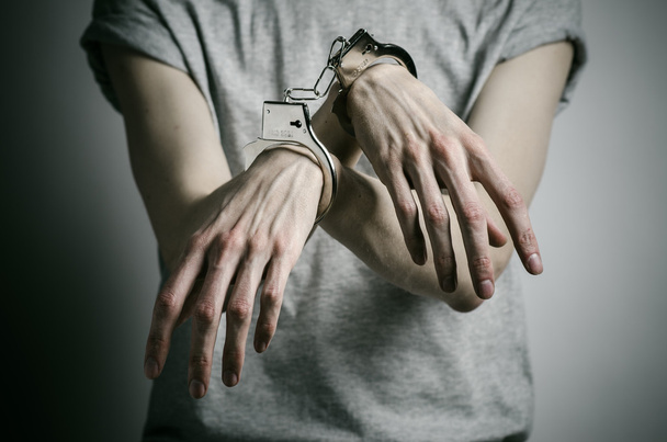 Prison and convicted topic: man with handcuffs on his hands in a gray T-shirt on a gray background in the studio, put handcuffs on rapist - Foto, imagen