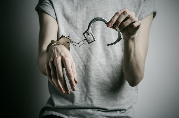 Prison and convicted topic: man with handcuffs on his hands in a gray T-shirt on a gray background in the studio, put handcuffs on rapist - Фото, изображение