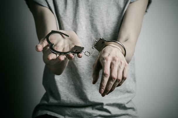 Prison and convicted topic: man with handcuffs on his hands in a gray T-shirt on a gray background in the studio, put handcuffs on rapist - Photo, Image