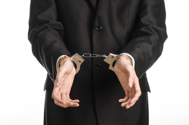 Διαφθορά και δωροδοκία θέμα: επιχειρηματίας σε ένα μαύρο κοστούμι με χειροπέδες στα χέρια του σε λευκό φόντο σε στούντιο απομονωθεί - Φωτογραφία, εικόνα