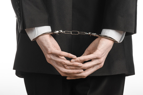 Corruption and bribery theme: businessman in a black suit with handcuffs on his hands on a white background in studio isolated - Foto, imagen