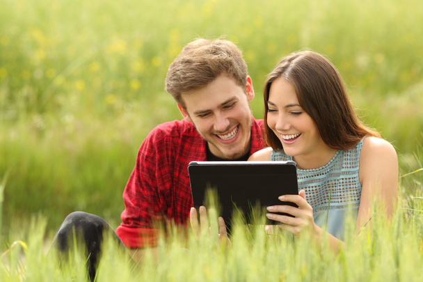 Couple watching videos in a tablet in a field - Foto, afbeelding