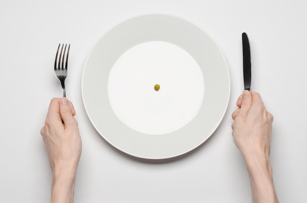 Healthy food theme: hands holding knife and fork on a plate with green peas on a white table top view - Foto, imagen