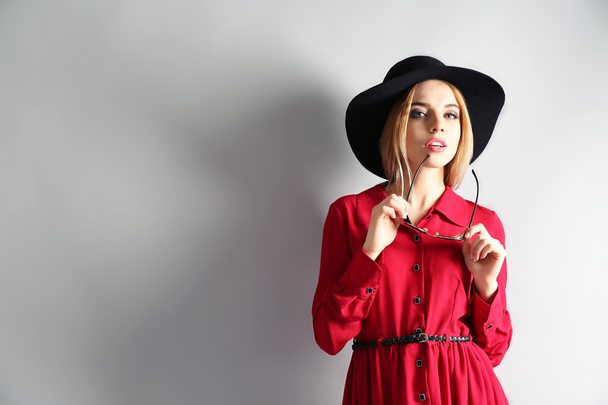 Expressive young model in red dress and black hat on gray background - Fotografie, Obrázek