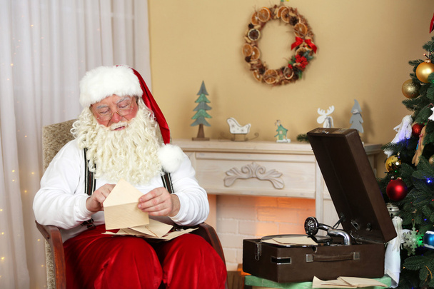 Santa Claus sitting with children letters in comfortable chair near fireplace at home - Foto, Imagen