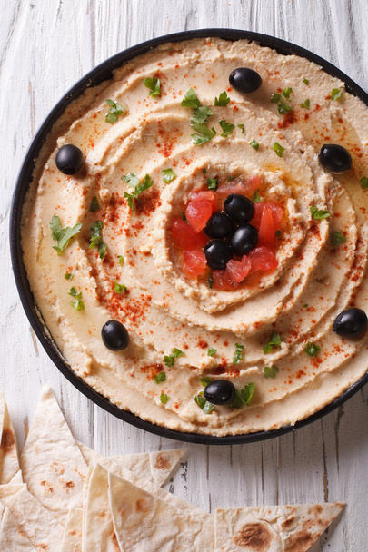 Hummus met olijven, tomaten en kruiden verticale bovenaanzicht - Foto, afbeelding