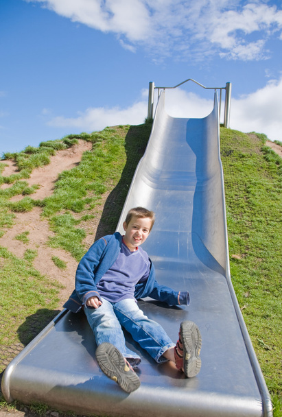 Little boy sliding down playground slide, some motion blur - Foto, afbeelding