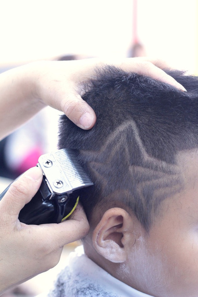 La coupe de cheveux du garçon avec tondeuse et rasoir dans le salon de coiffure
 - Photo, image