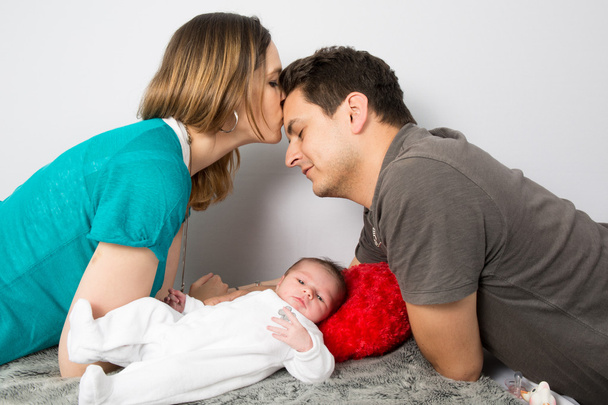 Stolze Eltern blicken auf ihre kleine Tochter und küssen sich - Foto, Bild