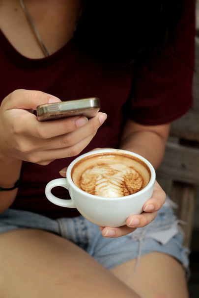 Vrouw drinken koffie in cup en slimme telefoons - Foto, afbeelding