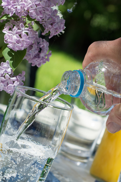 ruka vylévání vody z láhve do sklenice na zahradu  - Fotografie, Obrázek