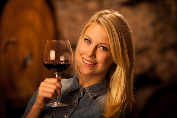 Beautiful young blond woman tasting red wine in a wine cellar - Fotoğraf, Görsel