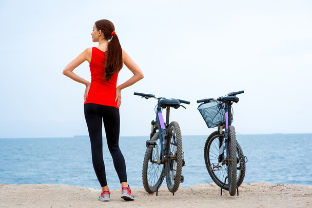 Спортивна жінка з велосипедами на пляжі
 - Фото, зображення