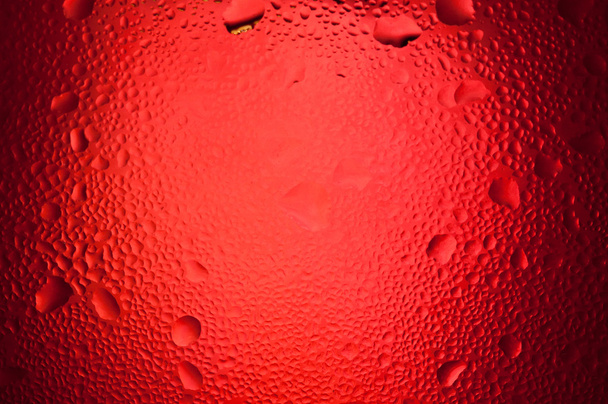 Wassertropfen auf rotem Hintergrund mit Scheinwerfermitte  - Foto, Bild