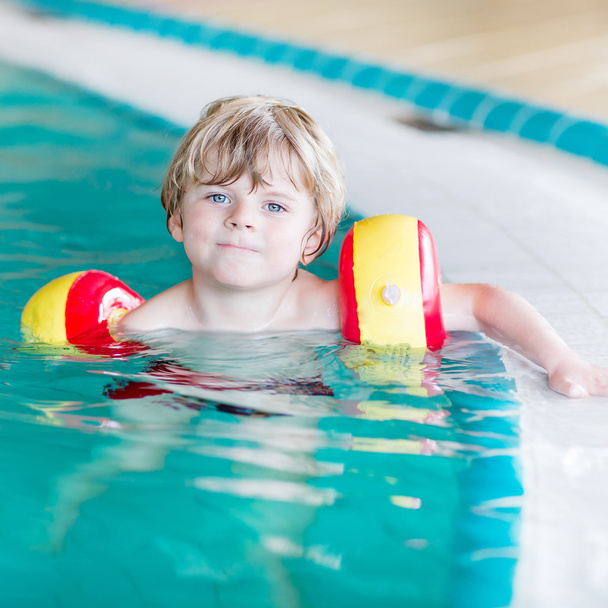маленький мальчик с пловцами учится плавать в закрытом бассейне
 - Фото, изображение