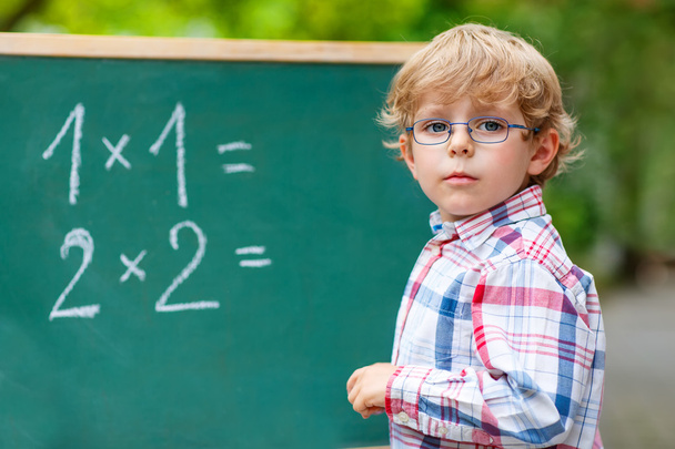 Niño preescolar con gafas en pizarra practicando matemáticas
 - Foto, Imagen