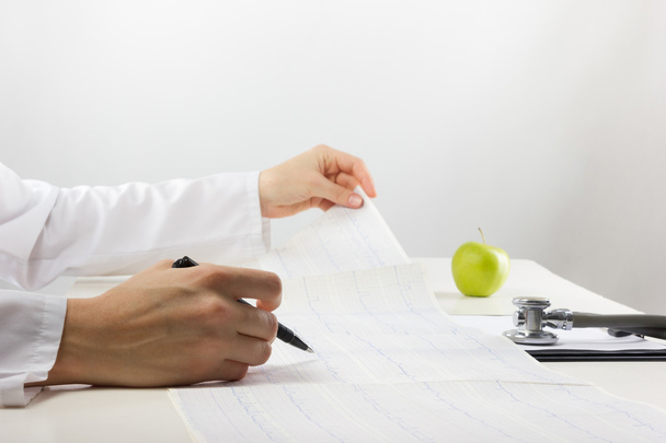 Doctor with medical stethoscope and green apple analyzing cardiogram results - Photo, Image