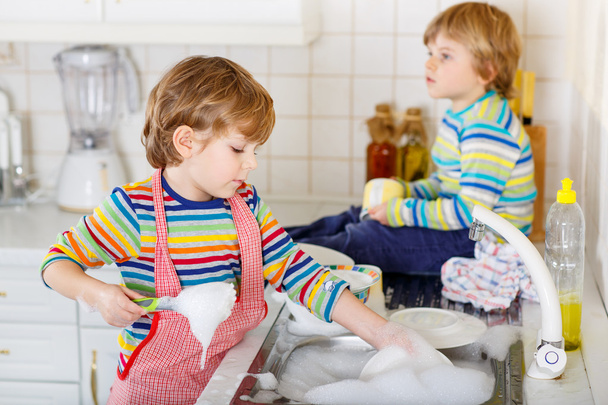 Two little blond kid boys washing dishes in domestic kitchen - Foto, Bild