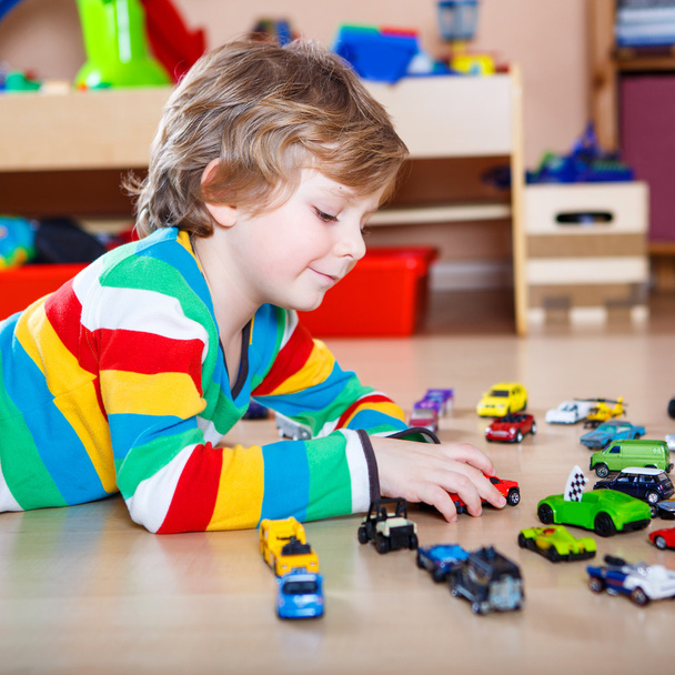 Boldog vicces kis szőke gyermek játszó rengeteg játékszert autók - Fotó, kép