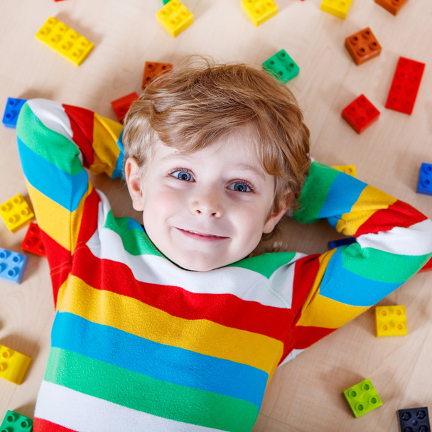 Little blond child playing with lots of colorful plastic blocks  - 写真・画像
