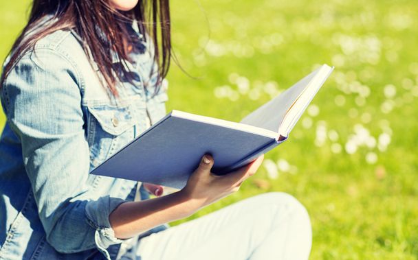close up of smiling young girl with book in park - Foto, Bild