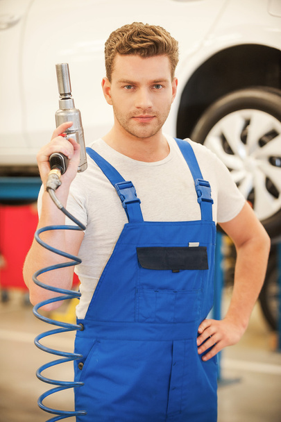 Mann mit Druckluftschlüssel in Werkstatt mit Auto im Hintergrund - Foto, Bild