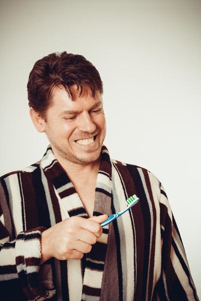 Młody człowiek w szlafrok szczotkowanie zębów, stonowanych - Zdjęcie, obraz
