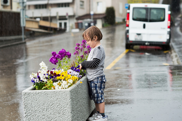 Милий маленький хлопчик грає під дощем у місті
 - Фото, зображення