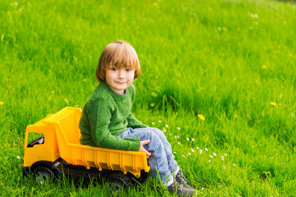 Schattige kleine jongen speelt met een grote gele speelgoedauto buiten - Foto, afbeelding