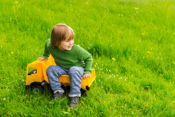 Schattige kleine jongen speelt met een grote gele speelgoedauto buiten - Foto, afbeelding