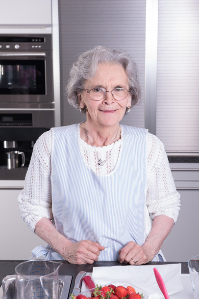 actieve vrouwelijke pensioen-of rentetrekker bereidt aardbeien in de keuken - Foto, afbeelding