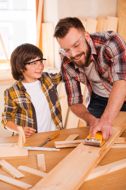 carpenter showing his son how to sand wood - Foto, afbeelding