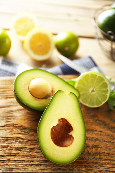 Sliced avocado and lemon lime on cutting board, on wooden background - Foto, afbeelding