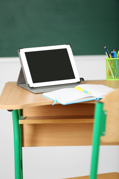 Wooden desk with stationery and tablet in class on blackboard background - Valokuva, kuva