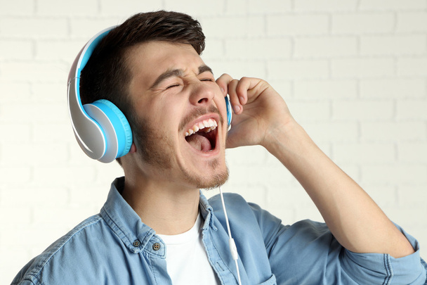 schöner junger Mann hört Musik auf Backsteinmauer Hintergrund - Foto, Bild