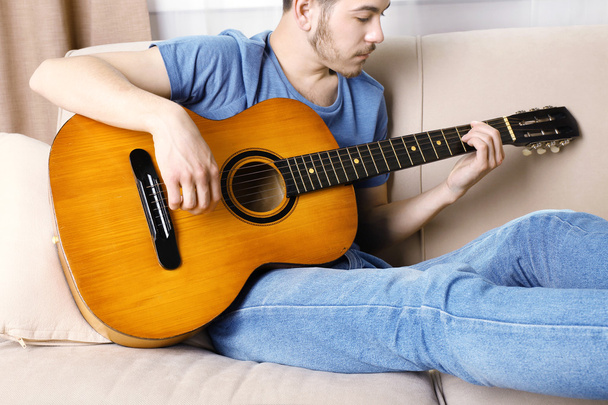 Young man with guitar on sofa in room - Фото, зображення