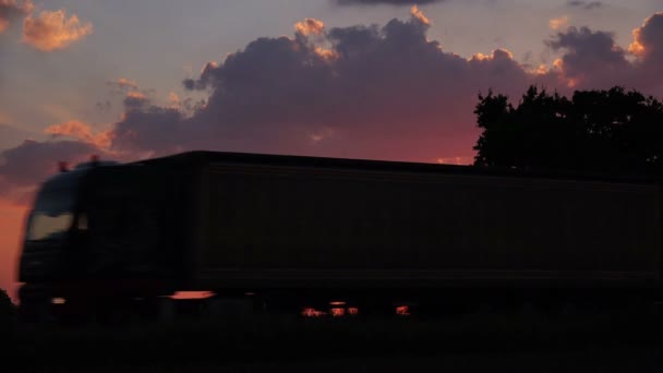 Samochodów ciężarowych sylwetka w wieczór zachód słońca przez wieś - Materiał filmowy, wideo