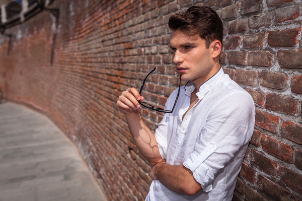 Pensive young fashion man holding his glasses - Foto, imagen