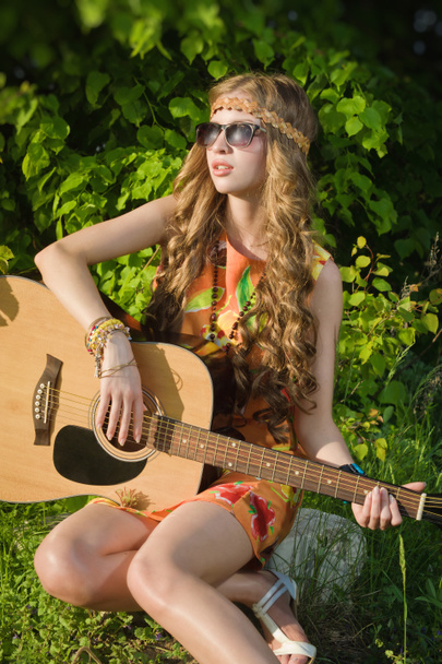jonge vrouw zittend op een veld en het spelen van gitaar - Foto, afbeelding