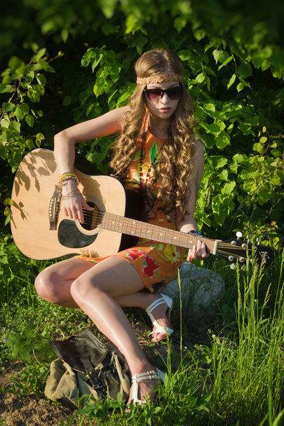 Young woman sitting on a field and playing guitar - Photo, Image
