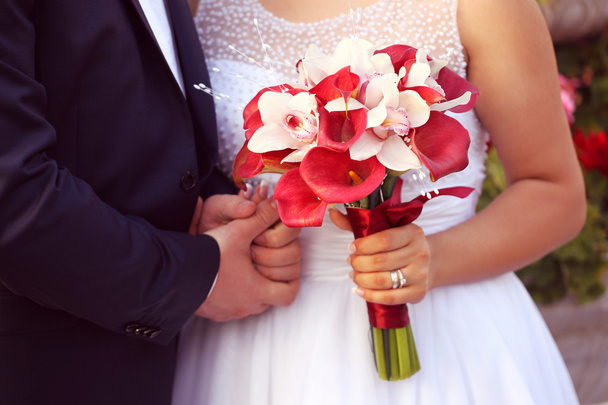 Hände eines Brautpaares. Braut mit rotem Lilienstrauß - Foto, Bild