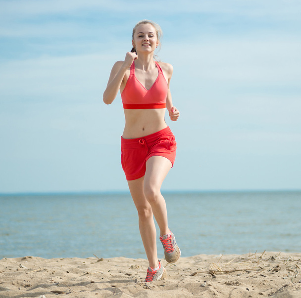 Young lady running at the sunny summer sand beach. Workout.  Jog - Фото, изображение
