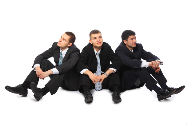 három fiatal üzletemberek padlón ül, és úgy néz ki minden irányba - Fotó, kép