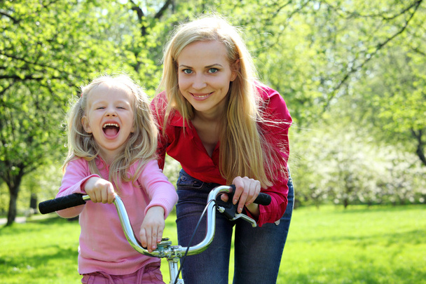 Laughing girl on bicycle with mother in spring garden - Fotó, kép