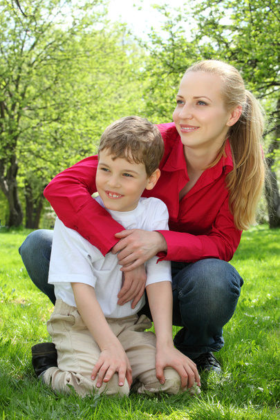 Mãe abraça atrás filho sentado no colo na grama no parque em
 - Foto, Imagem