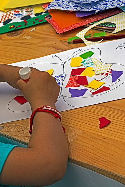 Ребенок, который склеивает вместе кусочки цветной бумаги
 - Фото, изображение