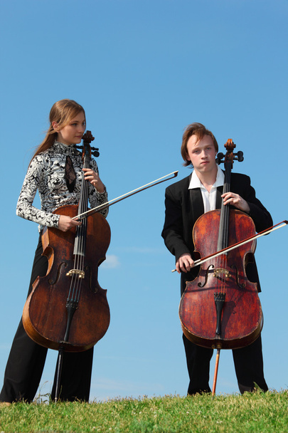 Two musicians play violoncellos against sky - Фото, изображение
