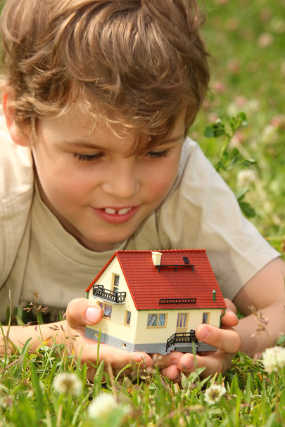 Boy lies in grass with house model in hands - Foto, Imagen